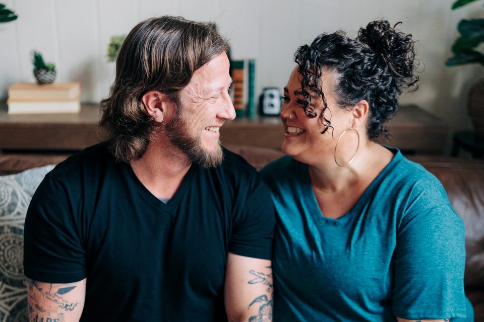 Adam and Alea Manning sitting and laughing together on a couch in their home
