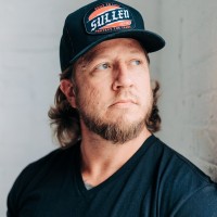 Adam Manning, calm and direct expression in a black t-shirt and ball cap